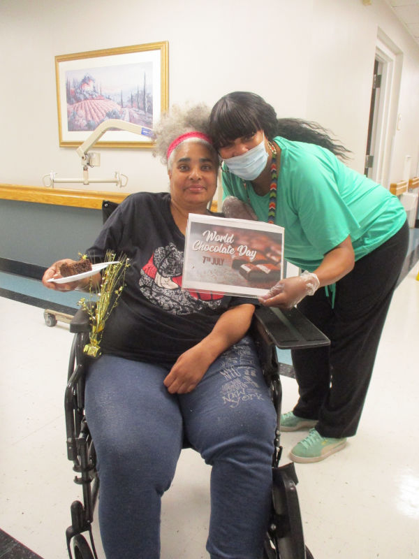 Woman in wheelchair holding plate with chocolate cake on it with another woman holding a World Chocolate Day sign